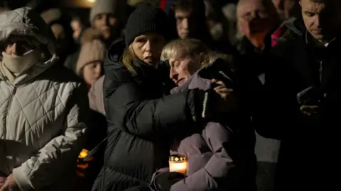 PA Media Two women comforting each other at a candle-light vigil 
