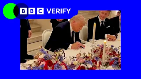 US President Donald Trump in Versailles as he signs a deal with Iran to end the war. French President Emmanuel Macron sits to his left. The blue BBC Verify logo is in the top left corner. 