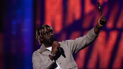 Reuters Myles Smith wears a white t-shirt with a grey jacket as he gives a speech and receives the Rising Star award at the Brit Awards at the O2 Arena in London, Britain, March 1, 2025.
