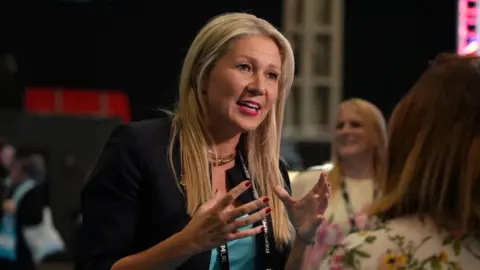 Sam Robinson/BBC Laura Anne Jones stood on the centre of the photograph talking to a woman stood to the right of her. Jones is wearing a black jacket and a teal top.
