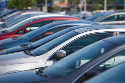 A number of cars in various colours are parked in a car park