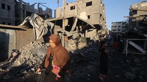 A Palestinian woman walks past damaged buildings after an Israeli strike on the Bureij refugee camp in the central Gaza Strip. Photo: 23 July 2025
