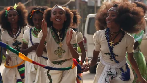 Orthodox Christian women clap as they walk down in traditional white outfits with silver cross necklaces in Mekelle in Ethiopia - archive shot