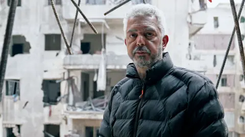 Middle-aged man, Mohammed, in ruins of wrecked apartment block