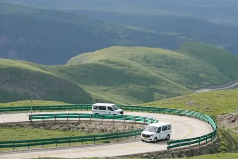 Getty Images A hilly landscape with grassy mounds and a winding road with green crash barriers on the side of the road