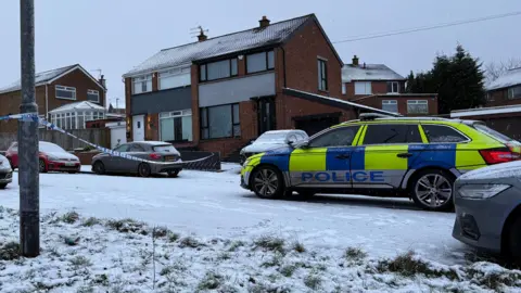 Police cordon and car outside a row of houses. Snow is on the ground.