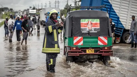 Getty Images A Kenyan firefighter gives directions people as they travel across a road heavily affected by floods following torrential rains in Kitengela, Kenya.