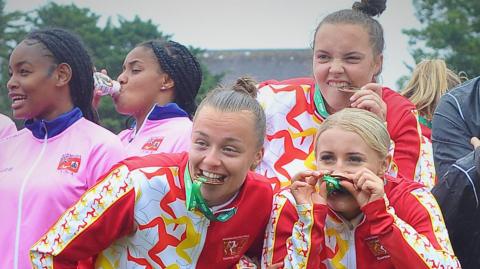 Manx footballers biting their bronze medal