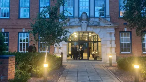 An entrance to the building is in the middle of the photo. Some people are visible inside.