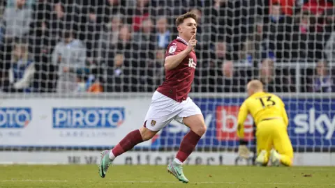 Sam Hoskins wears white shorts and a maroon football top, the colours of Northampton Town