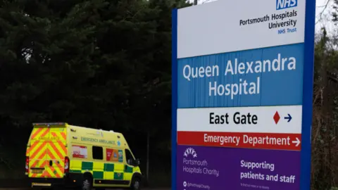 A hospital's emergency department sign with an ambulance in the background