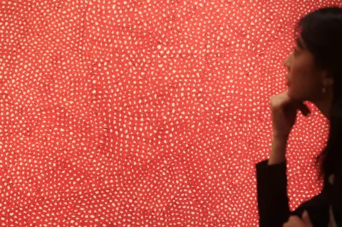 Getty Images A red and white patterned artwork filling the photo with a woman looking at it at the edge