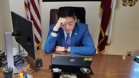 Gene Wu sits at his office desk, looking at a device in front of him