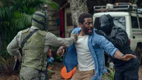 Netflix Ashley Thomas looking scared as two masked men push him