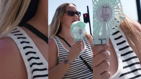 A woman cooling her face with a battery powered fan