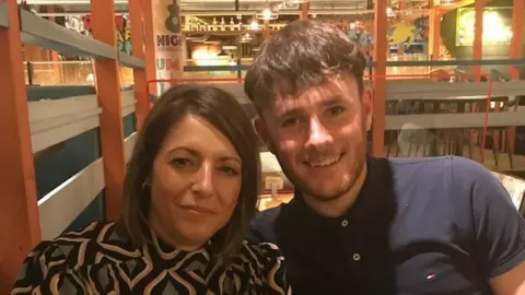 A woman in a leopard pattern dress sits next to a smiling man in a navy polo in a restaurant. 