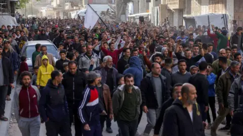 Wide angle photograph of hundreds of people walking through a street in Beit Lahia, northern Gaza as part of an anti-Hamas protest