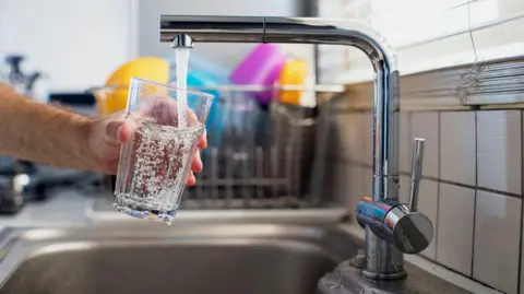 Getty Images A person holding a glass under a tap with water running from it. 