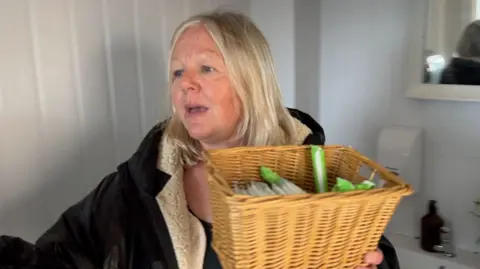 A woman inside a toilet carrying a wicker basket with sanitary ware inside.