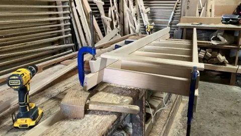 A partially made wooden ladden is sitting on a wooden work bench