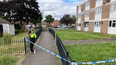 BBC A police officer guarding a cordon outside a block of flats.