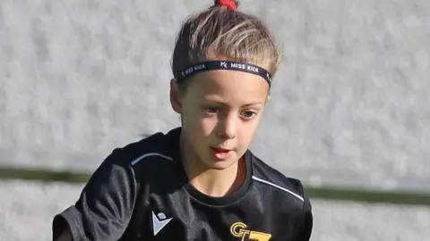 Poppy Atkinson is pictured standing in front of a stone wall. She is wearing a black sports top and has her hair tied up. There is a look of intent on her face.