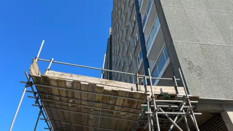 George Carden/BBC The tower block from the ground floor which has large panel walls and scaffolding around the edge 
