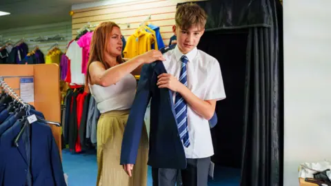 Getty Images A mother and teenage son shopping new clothes for school, trying on a school uniform