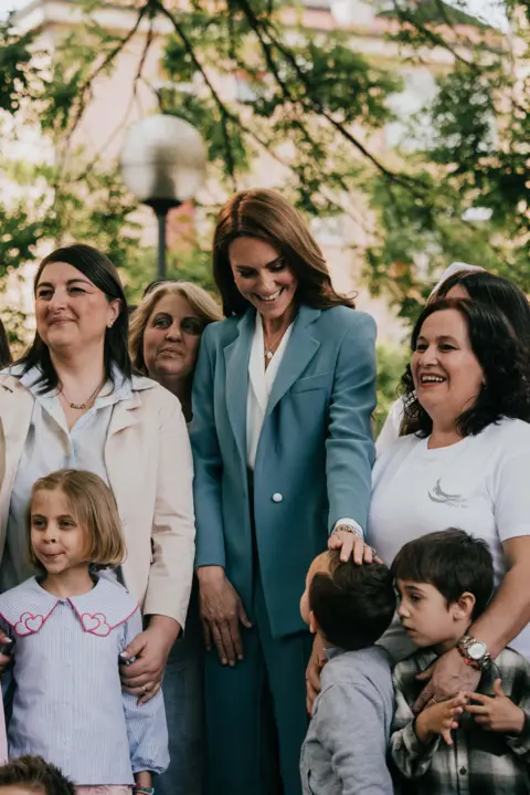 Royal Foundation Kate, wearing a blue trouser suit, surrounded by women and children
