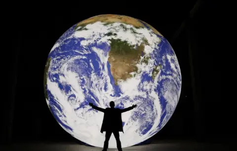Natural Environment Research Council A man holding his arms out in front of a giant illuminated earth