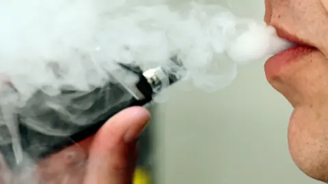 PA Media A cloud of smoke being blown by a man using a black vape device 