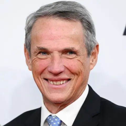 Getty Images Alan Hansen smiling at the camera. He has grey hair and is wearing a black jacket, white shirt and a  light blue tie with white squares on it