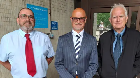 (Left to right) Michael Purkess, Chris Purkess and Richard Purkess stand side by side outside the glass-fronted entrance to Portsmouth Coroner's Court.