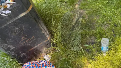 Jess Turnock A large metal grille is on grass next to an overflowing bin, with other pieces of rubbish nearby.