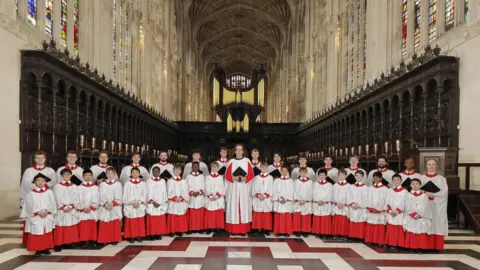 Leon Hargreaves/Choir of King's College Cambridge A group of choristers, boys and men, pose in the chapel. All are wearing white and red robes.