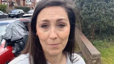 A woman with black hair stood in a street next to a red car