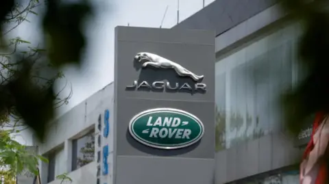 The silver leaping Jaguar emblem is on a grey pillar sign outside one of its factories, with the Land Rover badge below.