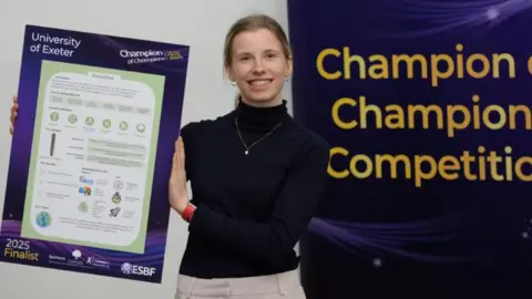 University of Exeter Kathryn Thomas wears a black top and has her hair tied back. She is holding a board displaying her award.