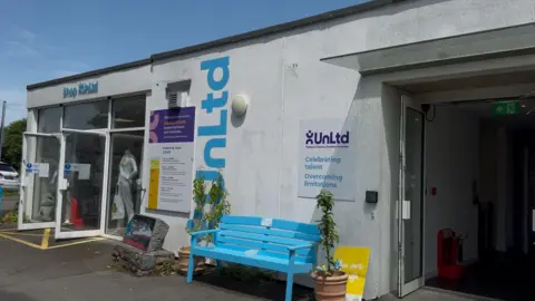 The exterior of the UnLtd building. It is white with a light blue bench and light blue signage.