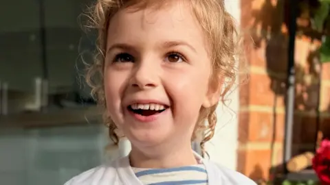 Ellis Russell A young girl with wavy blonde hair and brown eyes staring into the camera and smiling.