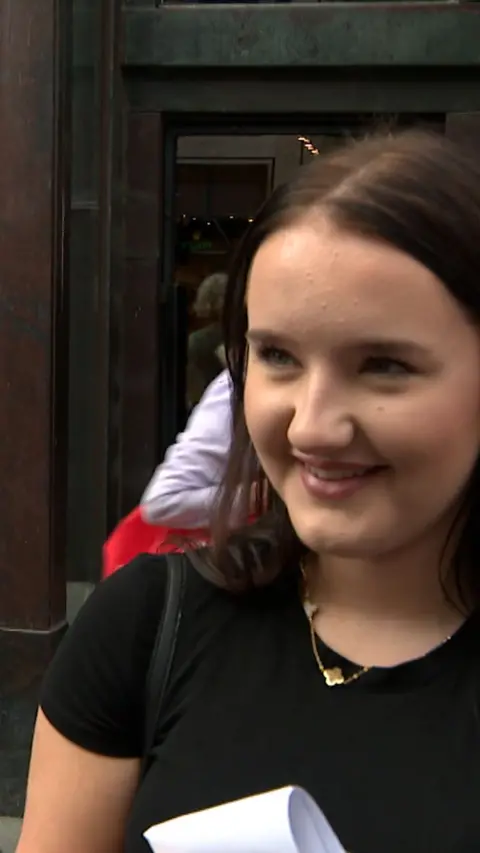 Girl with brown hair wearing black t-shirt smiling and looking to the left of the camera. 