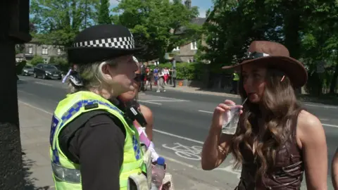 A police officer speaks to a woman who has a drink