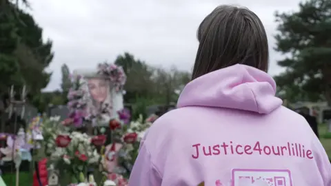 Debbie clack at the grave of her daughter with a pink hoody saying "Justice 4 our Lillie"