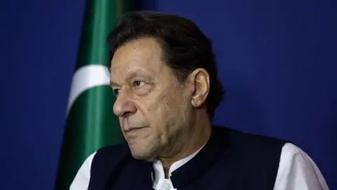 Imran Khan looking sombre with the Pakistan flag in the background