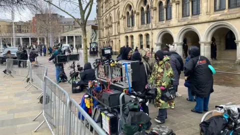 Camera and electrical equipment behind metal barriers in front of a historic town hall entrance 