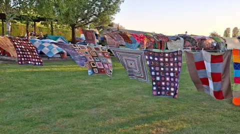 Fenland Woolly Hub Colourful handmade woollen blankets hang from washing lines in a field.