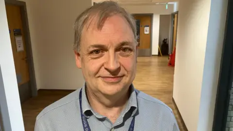 David Turner, looking at the camera, in a hospital corridor