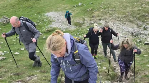 Contributed Mrs Blezard and her support team pictured climbing part of the mountain. They all are looking at the ground as they climb and some have walking poles.