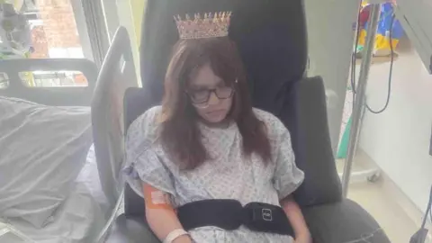 Natalie-Anne Rowlett Felicity-Jo in a chair in intensive care wearing a crown.