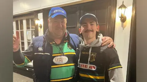 Chris Sansome and Matthew Sansome stand side by side with their arms over each other's shoulders. Both are wearing Northampton Saints jerseys.
